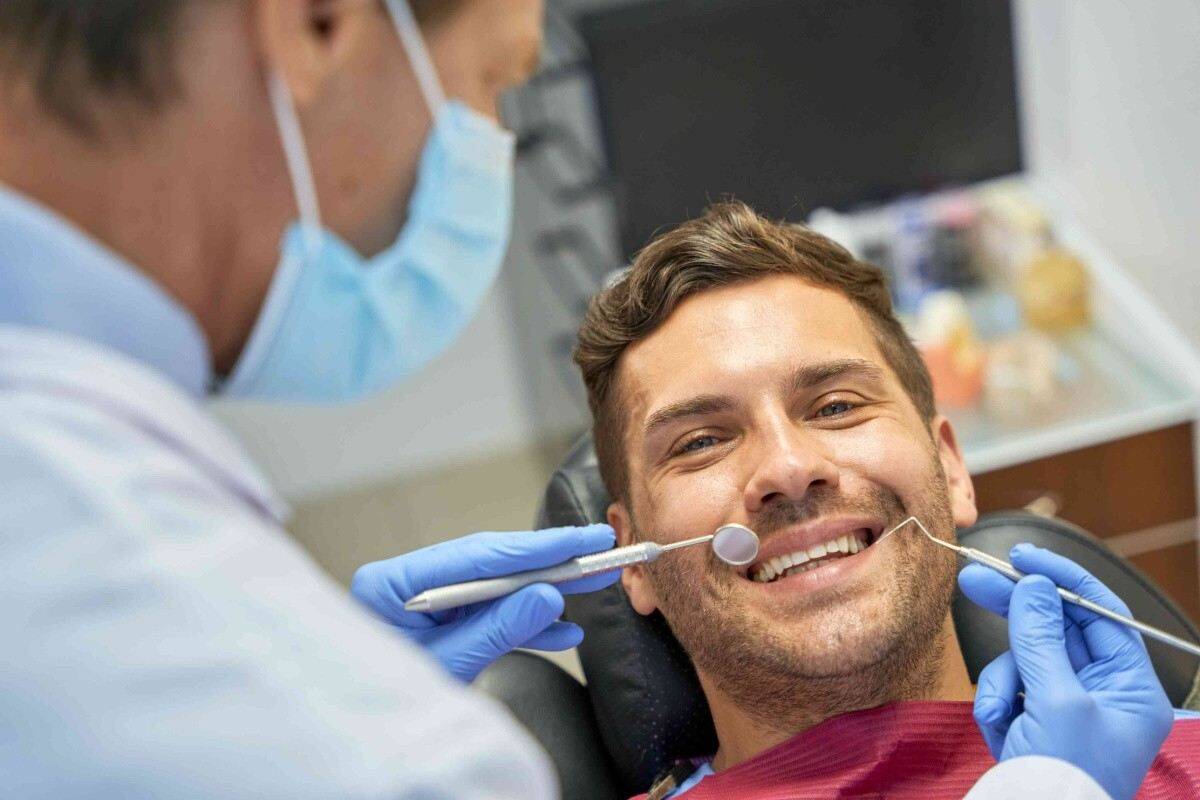 Dentist examining a smiling male patient with dental instruments during an orthodontic care visit