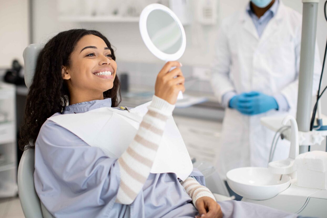 Smiling patient checking her smile with a hand mirror.
