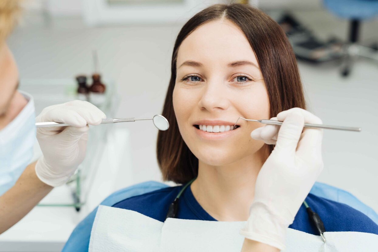 Dentist examining smiling patient's teeth with dental mirror