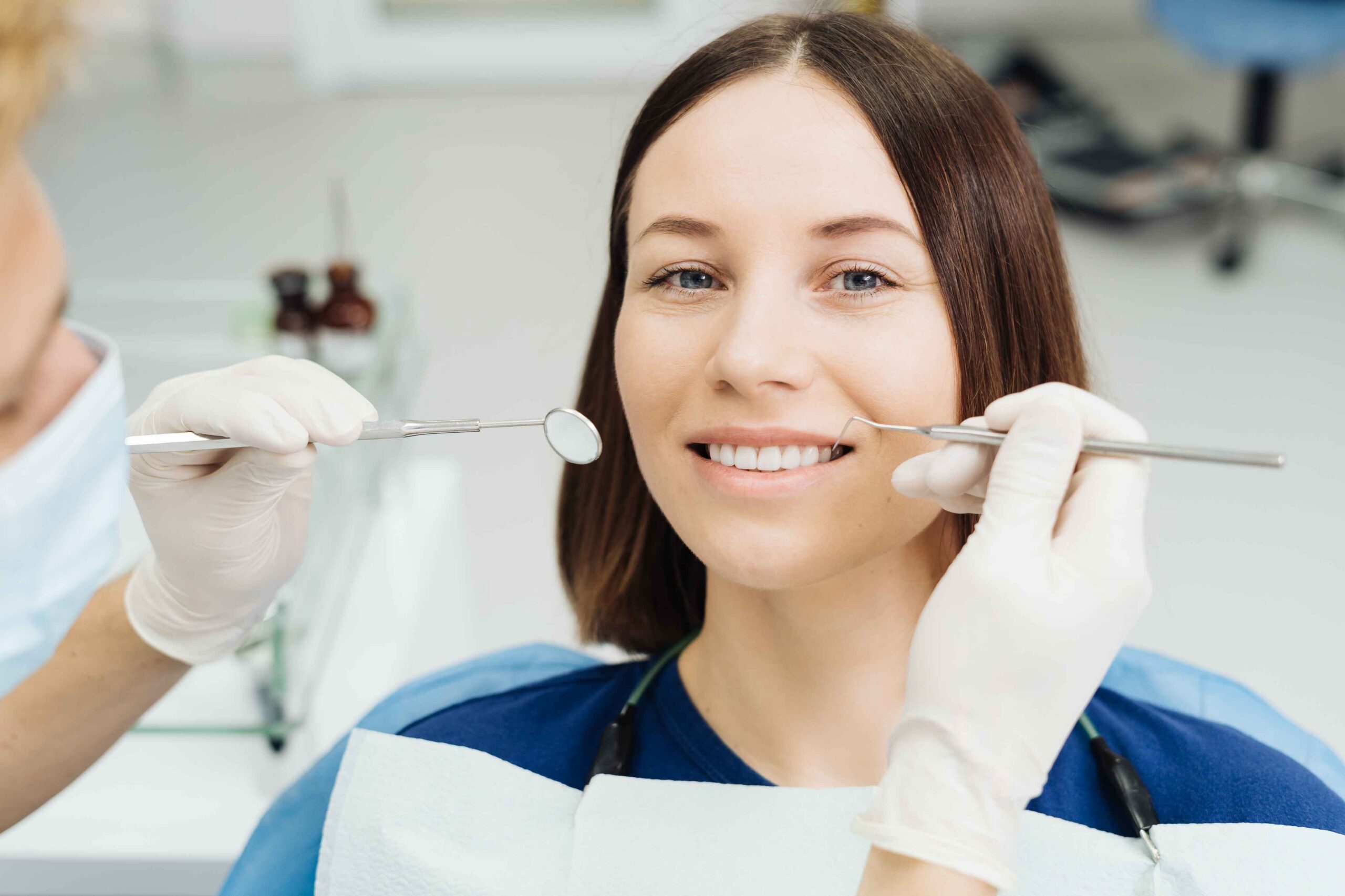 Dentist examining smiling patient's teeth with dental mirror
